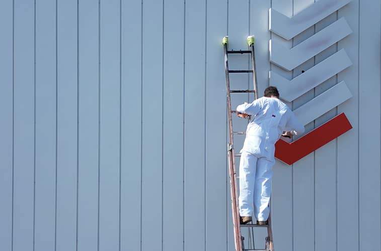 Professional commercial painter on a ladder painting a company sign
