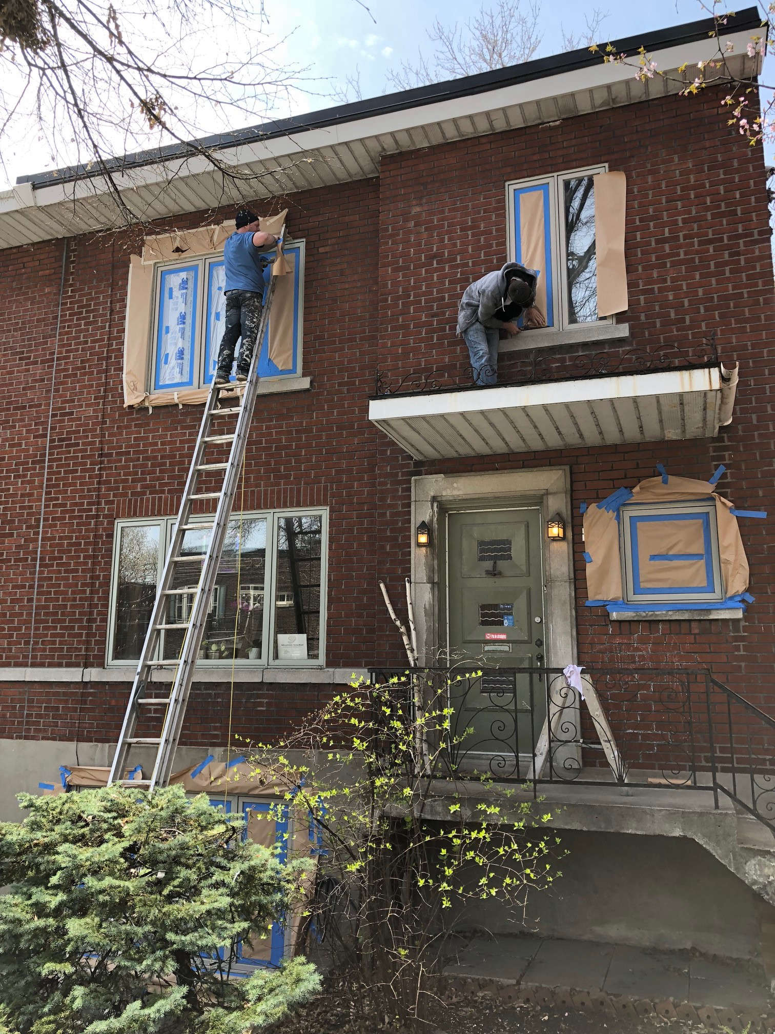 Two painters are preparing the windows of a brick building for painting