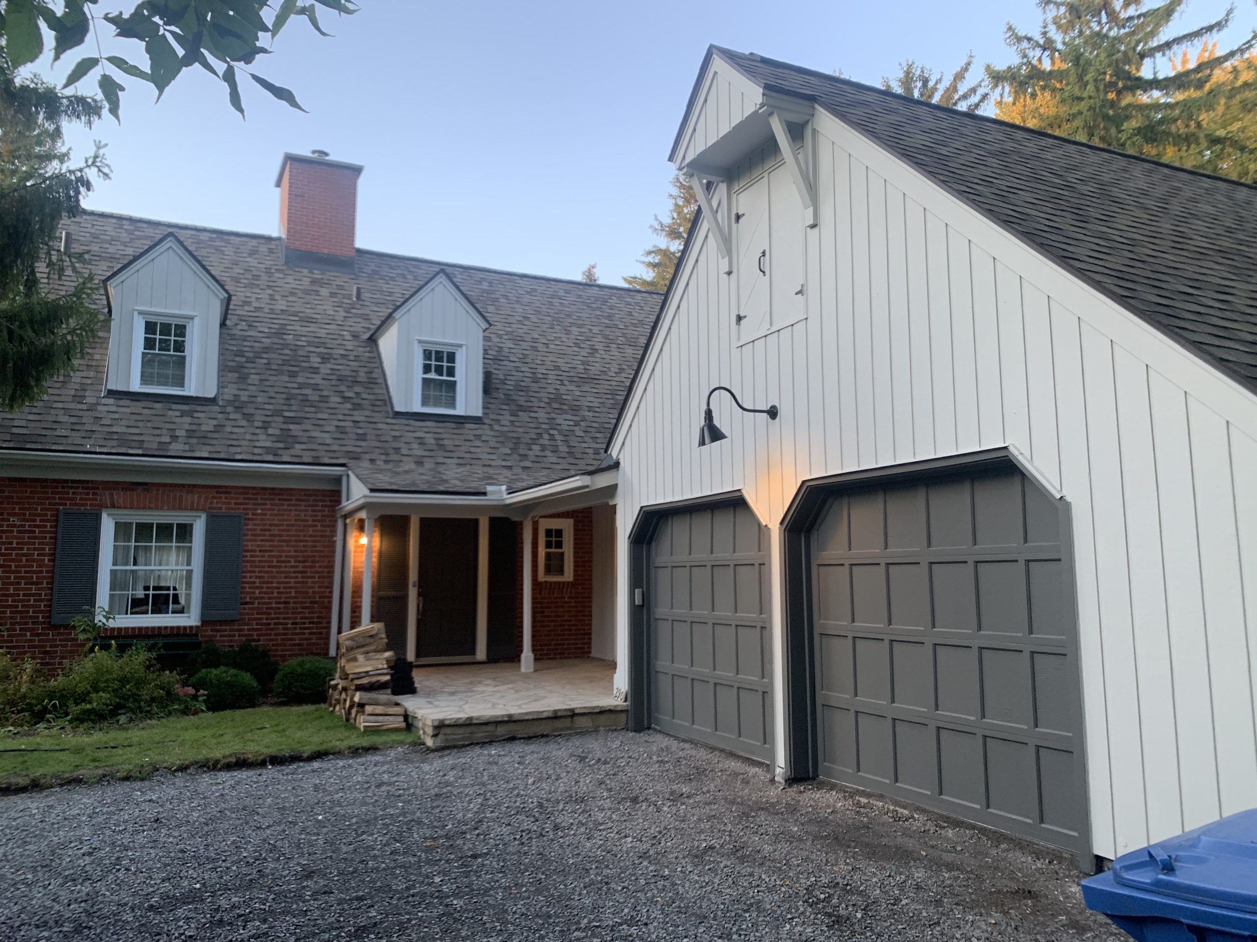 Maison avec 2 lucarnes et 2 portes de garage en bois et brique fraichement repeinte couleur taupe