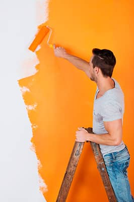 Une personne peinture un mur intérieur avec une peinture orange
